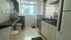 A modern kitchen with white cabinets, a black countertop, a stainless steel refrigerator, and a window providing natural light. - Family apartments - air conditioning, fan, internet... fully furnished. (Arraial do Cabo)