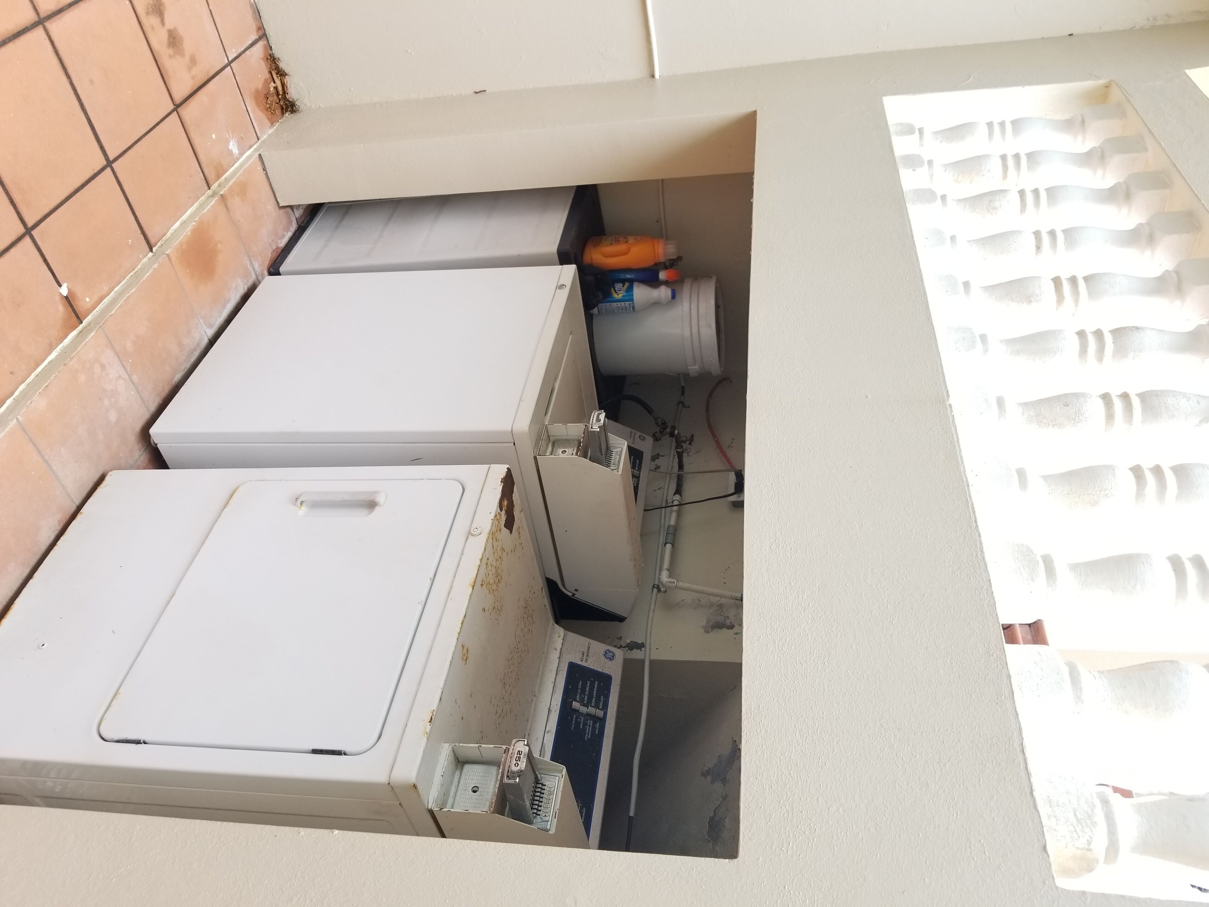 Ein Waschraum mit zwei weißen Waschmaschinen, einem Warmwasserbereiter und einem Bedienfeld.