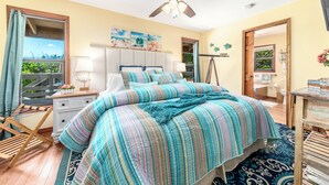 Une chambre à coucher comprenant un lit, un ventilateur de plafond, une table de chevet, une commode et une fenêtre avec des rideaux.