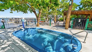 Une piscine avec un panier de basketball, entourée de palmiers et dotée d’une terrasse en bois.