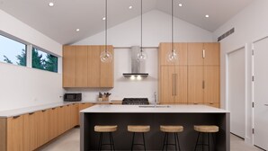 A modern kitchen with wooden cabinets, a central island with stools, and pendant lighting.