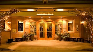 A hotel entrance with a warm, illuminated facade, double doors, and a brick-paved entrance area.