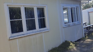 Un bâtiment d’un seul étage, doté de deux fenêtres, d’un toit plat et d’une zone de terrain non aménagée.
