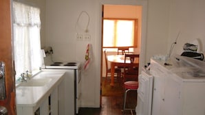 Une cuisine compacte équipée d’un évier, d’une cuisinière et d’un réfrigérateur. On aperçoit une table à manger avec des chaises au fond.