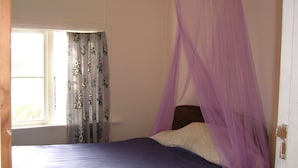 Une chambre à coucher avec un lit, un baldaquin violet, des rideaux à motifs floraux et une fenêtre.