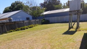 Une cour verdoyante avec une clôture en bois, un abri en métal et un bâtiment blanc doté d’un garage.