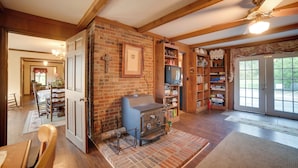 A cozy living room with a fireplace, wooden beams, and a television. - Dayton Home w/ Pool & Deck on 37 Private Acres! (Dayton)