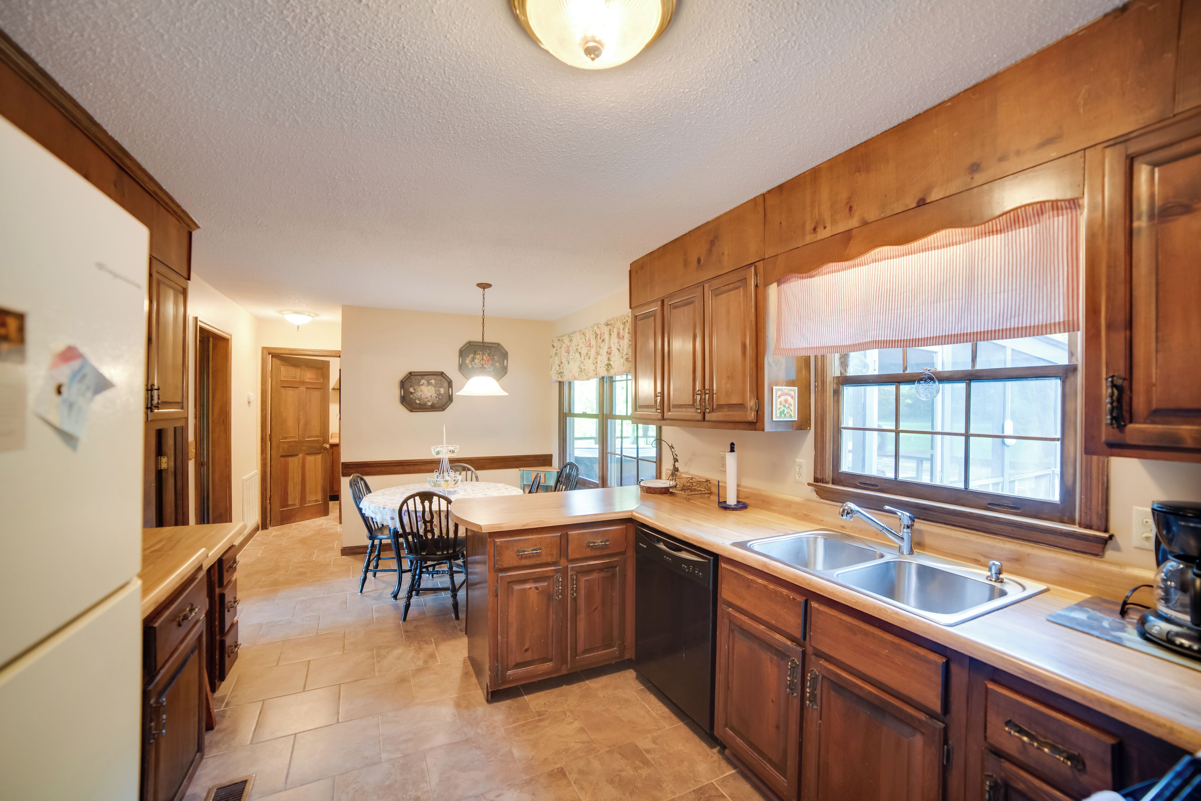 Una cocina con armarios de madera, una isla central, un fregadero y una zona de comedor con sillas.
