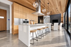 A modern kitchen with a central island, bar stools, and a dining area with a TV.