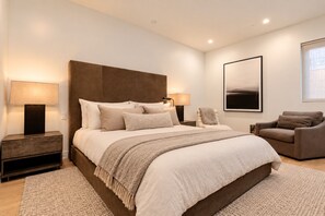 A modern bedroom with a large bed, two bedside tables, a chair, and a framed picture on the wall.