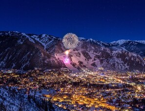 Eine verschneite Bergstadt bei Nacht mit einer großen Feuerwerksvorstellung.