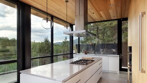 Une cuisine moderne dotée d’un grand îlot central, d’un plafond en bois et de grandes fenêtres offrant une vue sur l’extérieur.