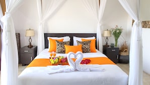 A four-poster canopy bed with white bedding, orange accents, and a heart-shaped towel arrangement. - Zara The Bali Ocean View (Badung)
