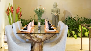 A dining area with a glass-top table, grey upholstered chairs, and a central wooden table base. - Zara The Bali Ocean View (Badung)