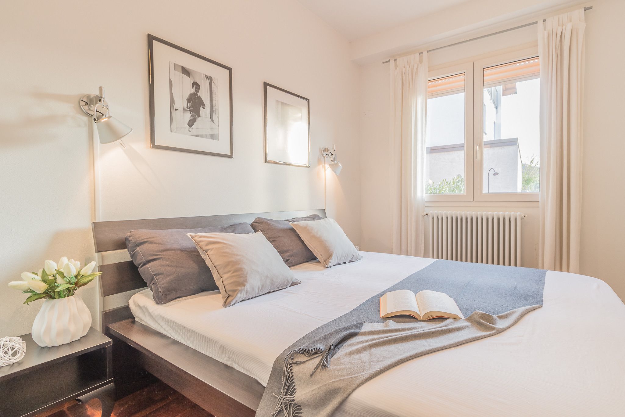 Ein ordentlich bezogenes Bett mit Kissen, ein Nachttisch mit Lampe und ein gerahmtes Bild an der Wand.