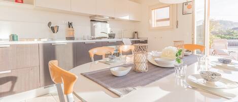 Een moderne keuken met witte kasten, een eethoek met een ronde tafel en uitzicht op de omgeving.