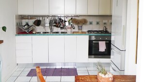 A kitchen with white cabinets, a stove, an oven, and a dining table with a placemat. - A full immersion in paradise (Vietri sul Mare)