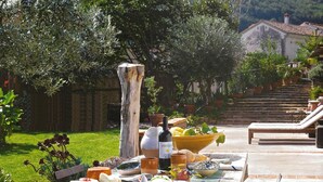 An outdoor dining area with a table set for a meal, surrounded by greenery and a building in the background. - A full immersion in paradise (Vietri sul Mare)