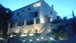 Un edificio de dos pisos con balcón y un pequeño jardín con plantas en macetas.