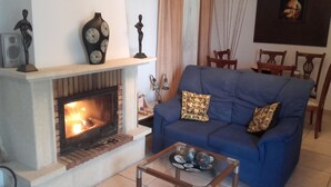 Una sala de estar con chimenea, sofá azul, almohadones decorativos y una mesa de centro de vidrio.
