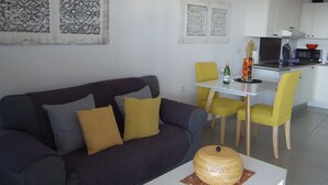Una sala de estar moderna con un sofá de color oscuro, sillas amarillas y una pequeña mesa de comedor.