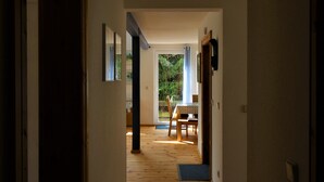 En hall som leder till en matplats med ett bord och stolar, trägolv och utsikt över grönområden utanför.
