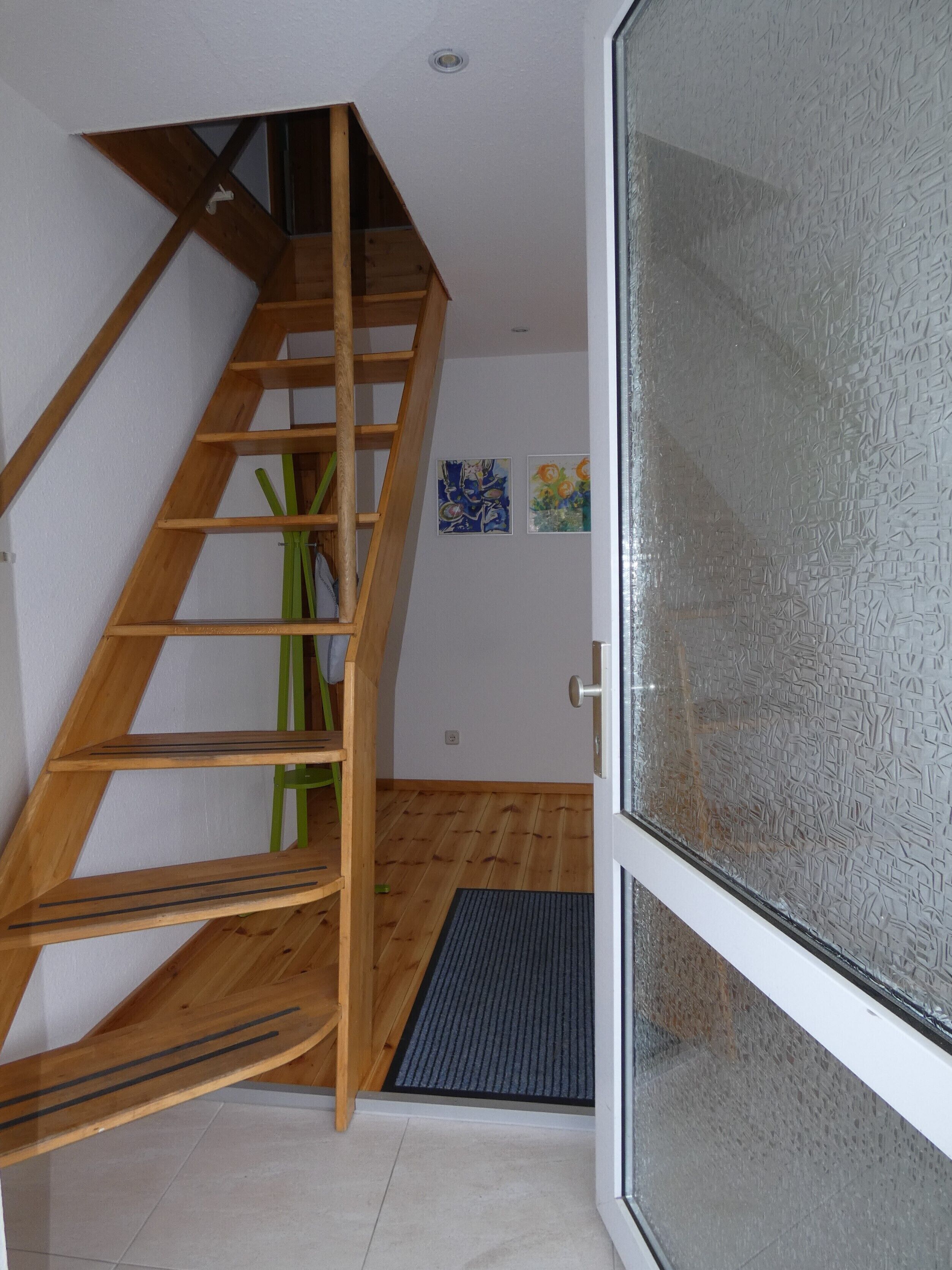 A wooden staircase leading to an upper floor, a glass door with a textured pattern, and two small artworks on the wall.