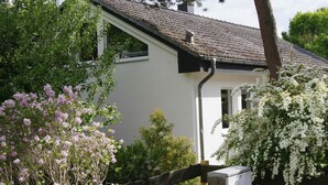 Ett vitt hus med ett tak täckt av tegelpannor, omgivet av blommande buskar.