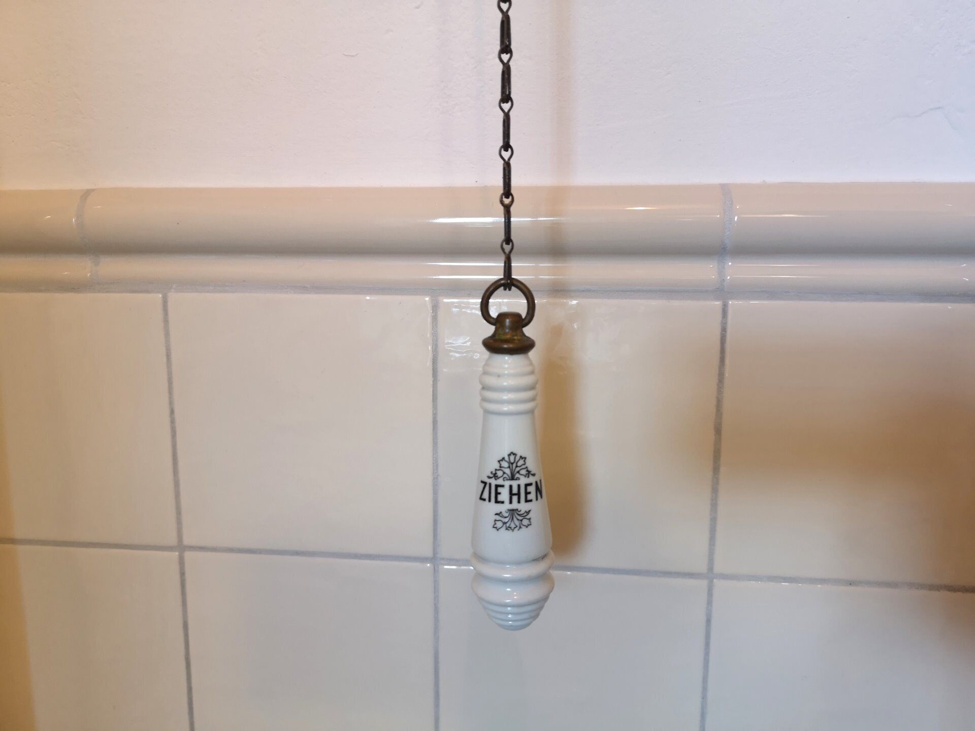 A white ceramic bottle with the inscription "ZIEHEN" hanging on a tiled wall.