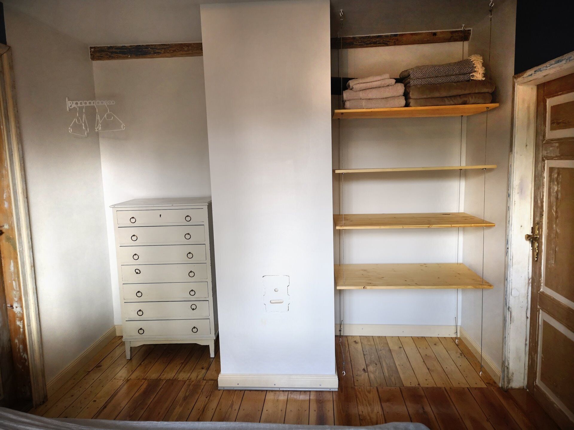 A room with a white dresser, a wooden floor, and a closet with shelves.
