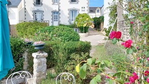 Une cour avec un bâtiment blanc, un banc en pierre et un rosier.