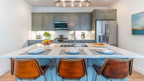 Una cocina moderna con una isla central, taburetes de bar y una lámpara colgante.
