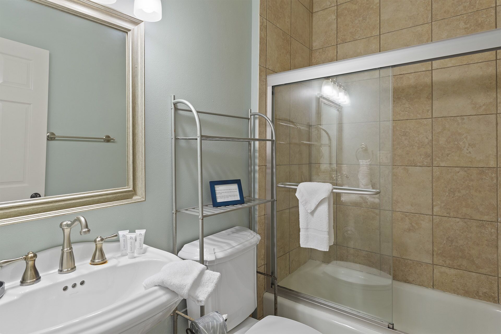 A bathroom with a sink, mirror, towel rack, and a glass-enclosed shower.