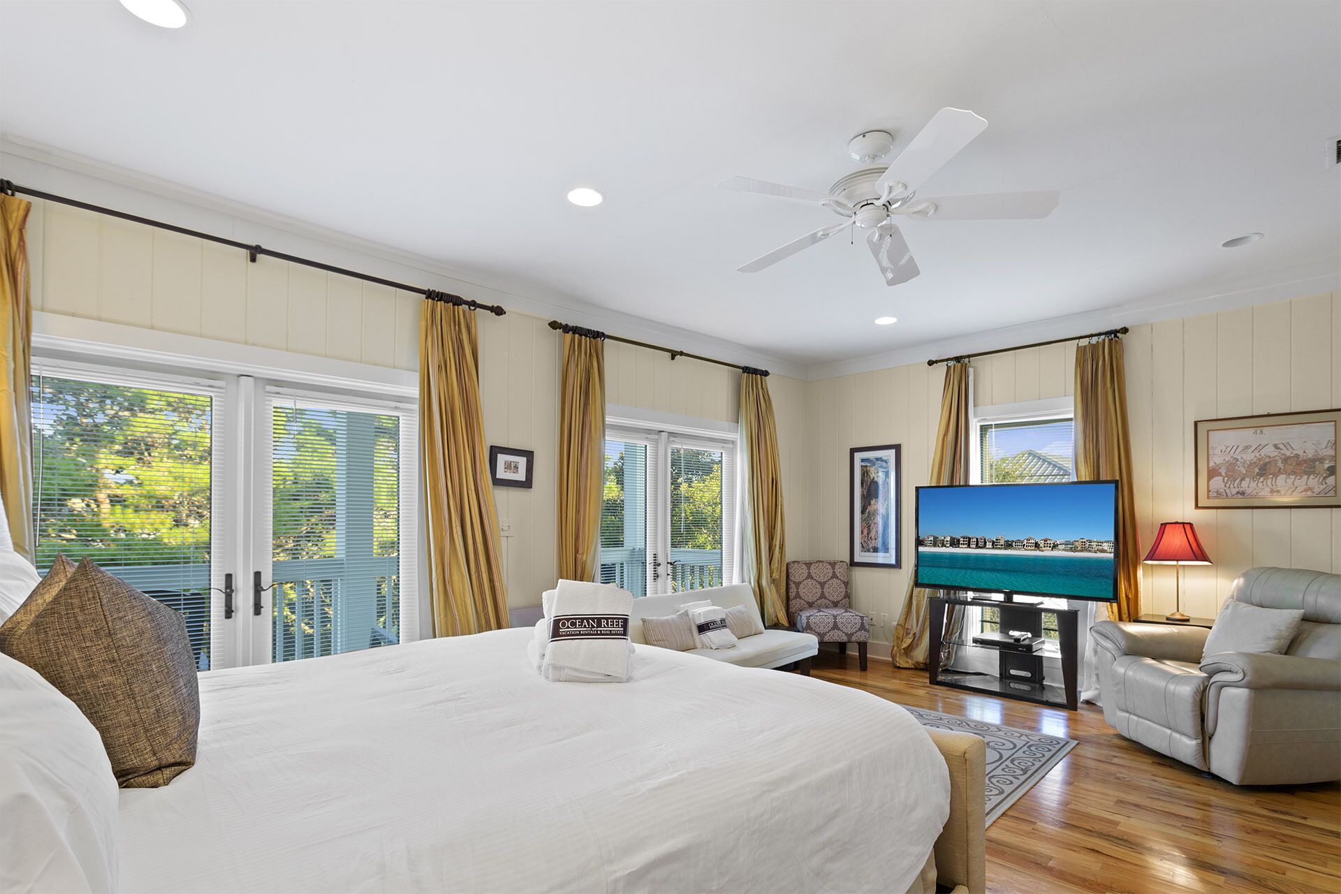 Una camera d'albergo con un letto grande, una ventola a soffitto, una TV e un'area salotto con una sedia e un divano.