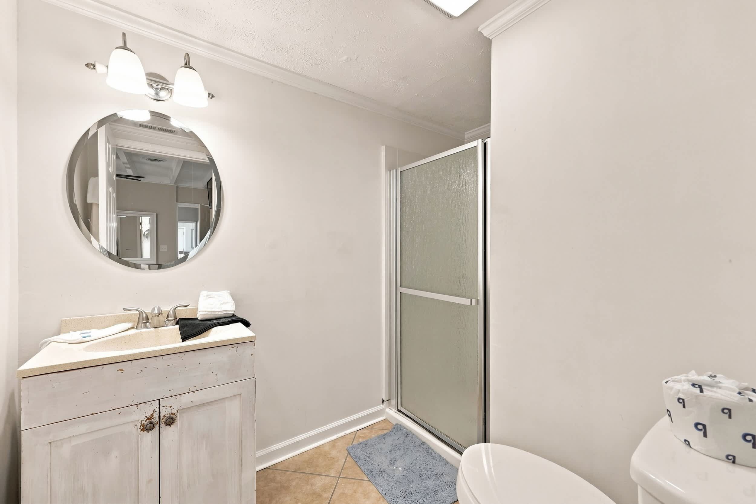A bathroom with a round mirror, a sink with a towel, a toilet, and a shower area.