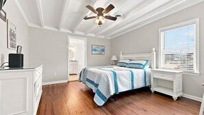 A bedroom with a wooden floor, a bed with a blue and white quilt, a ceiling fan, and a window with blinds. - Hazels Child Oceanfront Large  Beach House (North Myrtle Beach)