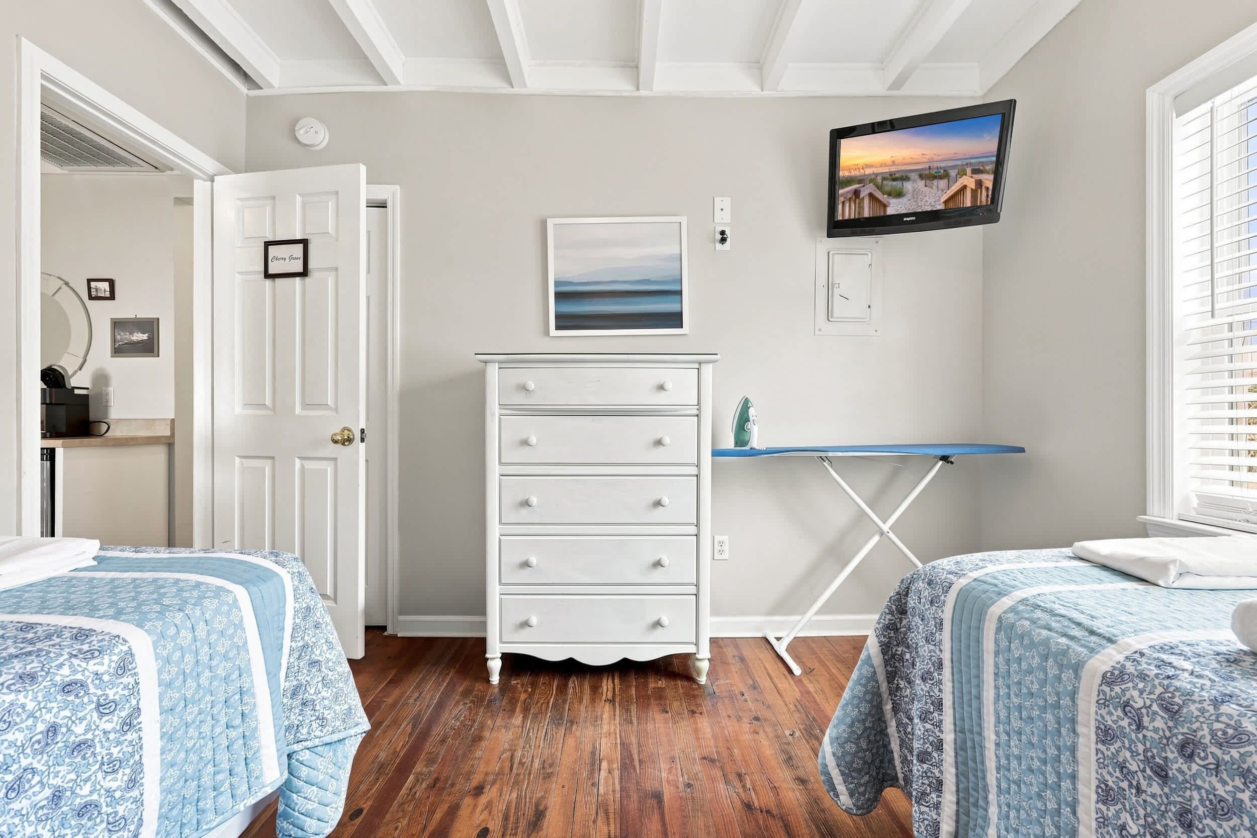 A bedroom with two beds, a dresser, a television, and a window with blinds.
