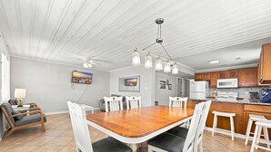 A spacious dining area with a wooden table and white chairs, a kitchen with wooden cabinets and modern appliances, and a ceiling with exposed beams. - Hazels Child Oceanfront Large  Beach House (North Myrtle Beach)