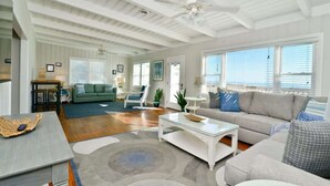 A spacious living room with a high ceiling, a large window, and a ceiling fan. - Hazels Child Oceanfront Large  Beach House (North Myrtle Beach)