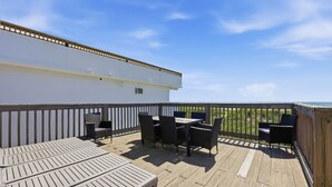 A wooden deck with outdoor furniture, including a table and chairs, overlooking a grassy area. - Hazels Child Oceanfront Large  Beach House (North Myrtle Beach)