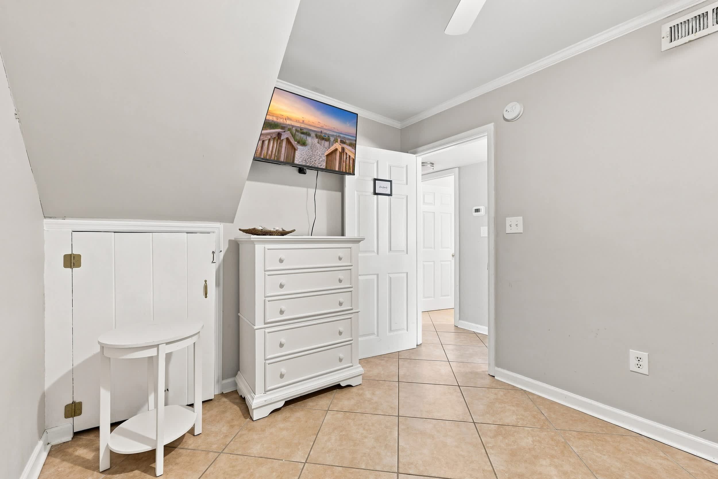 A hallway with a white dresser, a small table, and a television mounted on the wall.