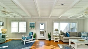 A spacious living room with hardwood flooring, a white ceiling, and a large window. There are two sofas, a coffee table, and a small side table. - Hazels Child Oceanfront Large  Beach House (North Myrtle Beach)