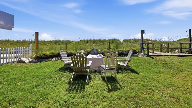 An outdoor seating area with a table and chairs, surrounded by a white picket fence and greenery. - Hazels Child Oceanfront Large  Beach House (North Myrtle Beach)