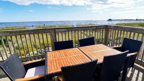A wooden deck with a table and chairs, overlooking a beach and a pier. - Hazels Child Oceanfront Large  Beach House (North Myrtle Beach)