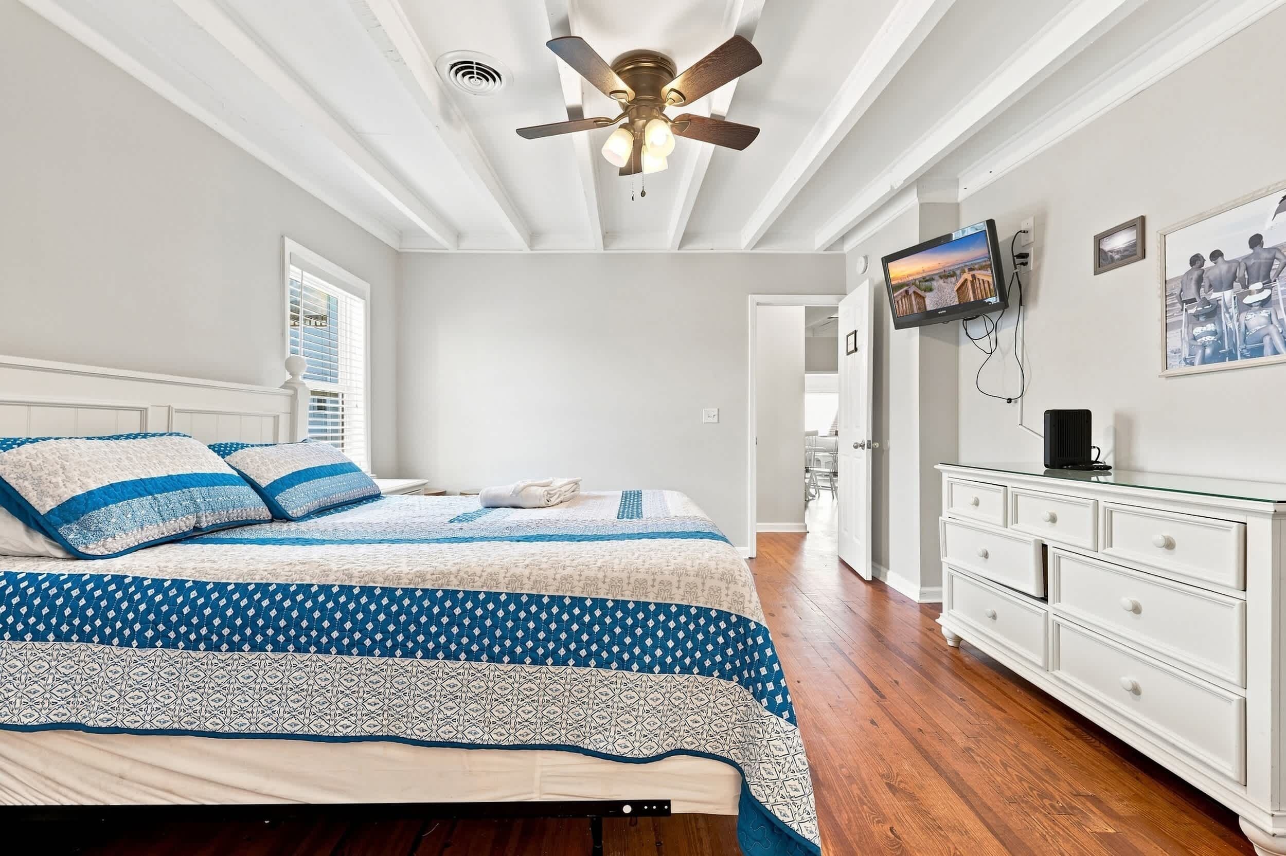 A bedroom with a bed, a ceiling fan, a TV, and a dresser.
