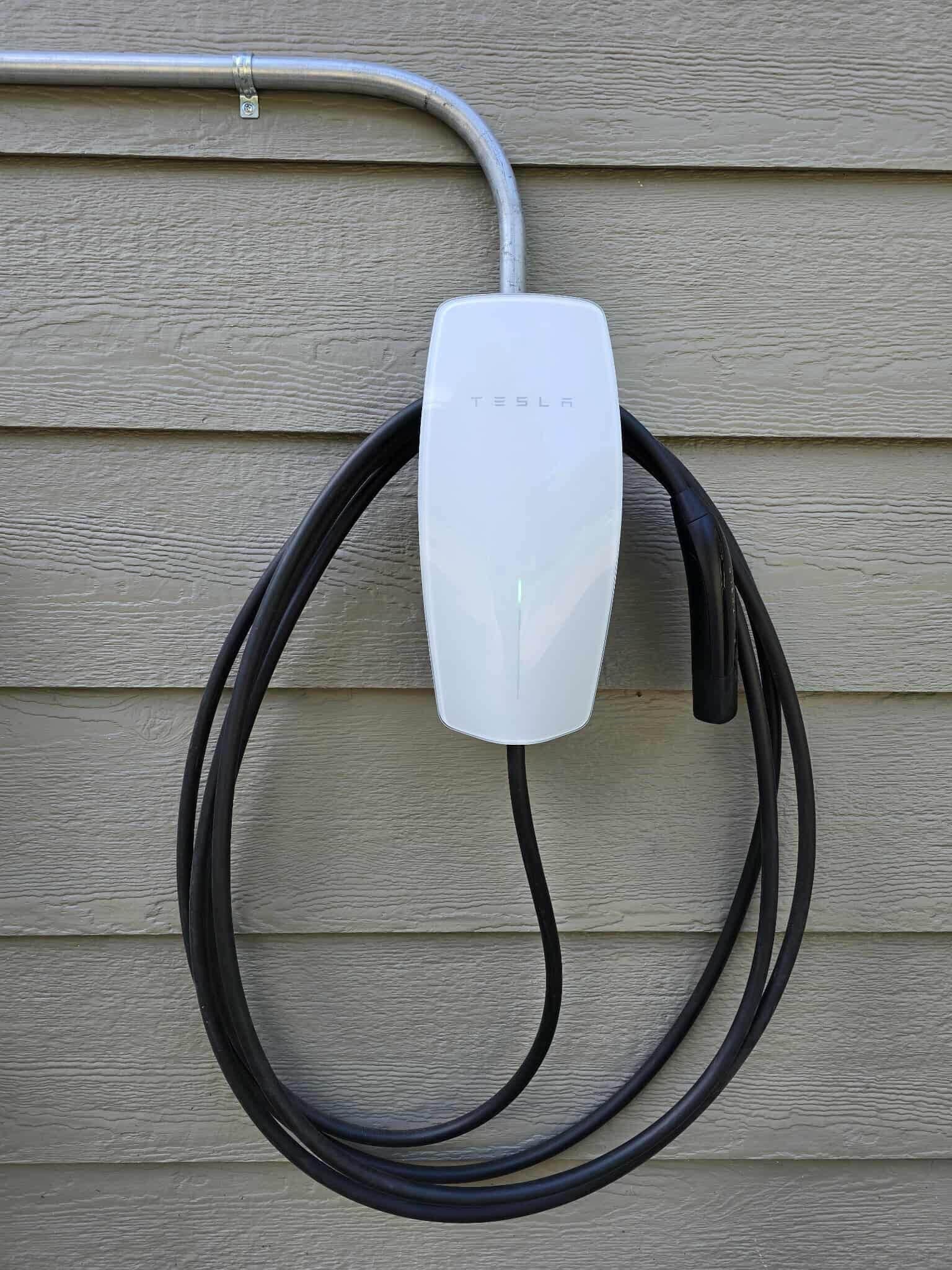 Une borne de recharge Tesla fixée sur un mur de maison.