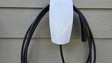 Une borne de recharge Tesla fixée sur un mur de maison.
