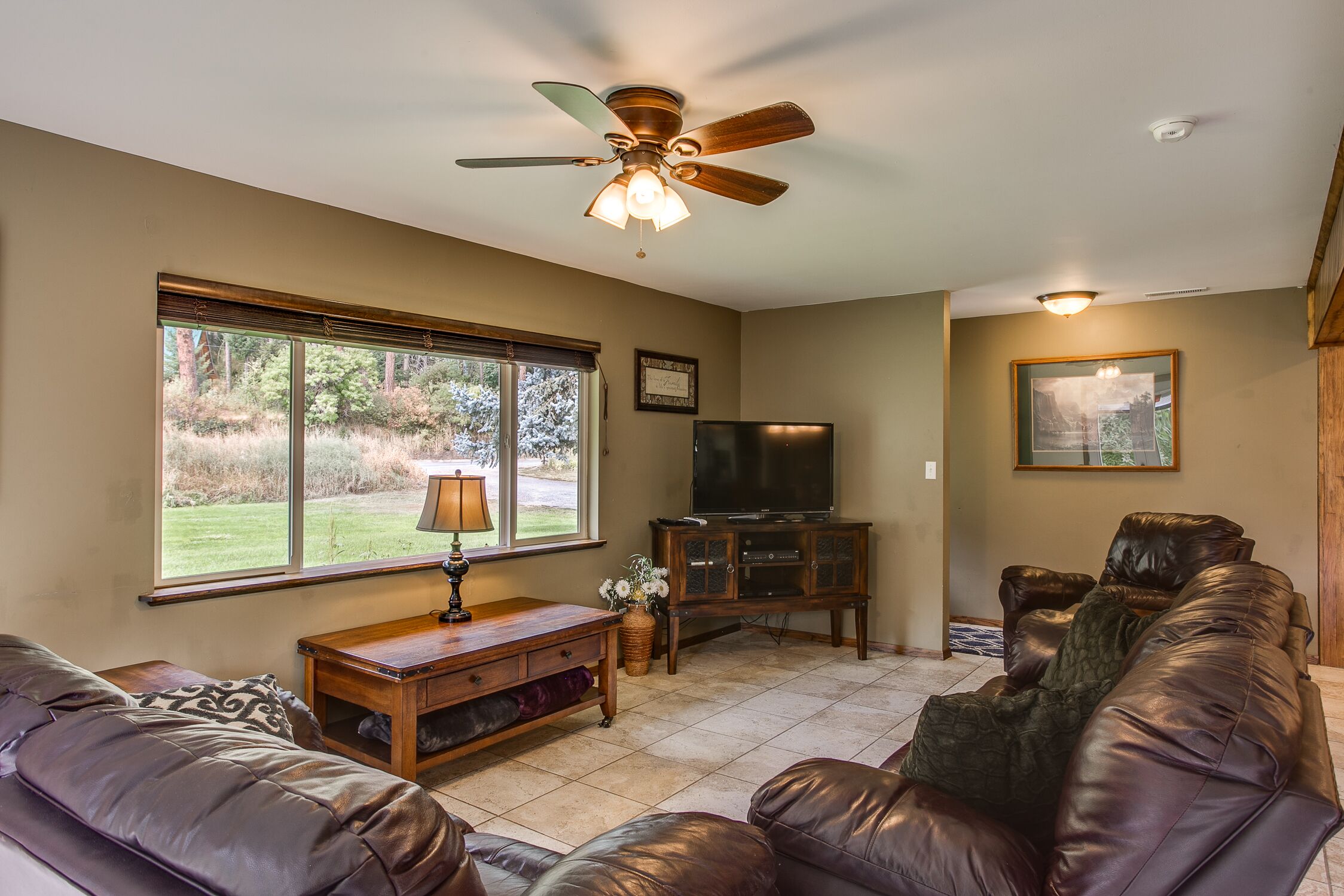 A living room with a brown leather sofa, a wooden coffee table, a TV stand, and a ceiling fan.