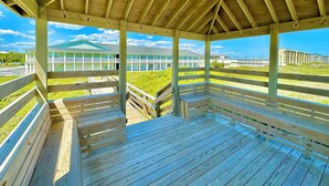 Una terraza de madera con bancos, un espacio cubierto con techo inclinado y vistas a un edificio con varios balcones.