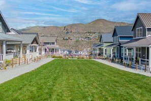 A row of modern houses with a grassy lawn in the foreground and a hilly landscape in the background.